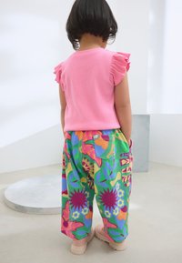 Rosa geripptes Oberteil mit Rüschensäumen, kombiniert mit mehrfarbigen, weit geschnittenen Hosen mit großen Blumen- und geometrischen Mustern.