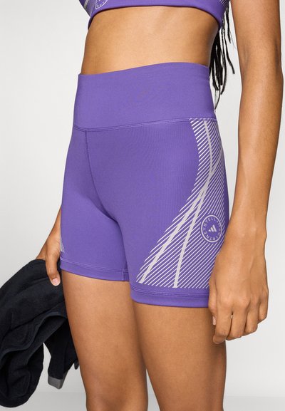 Lila sportos rövidnadrág sima, rugalmas anyagból. Finom fehér átlós csíkokkal és egy kerek logóval az oldalon.