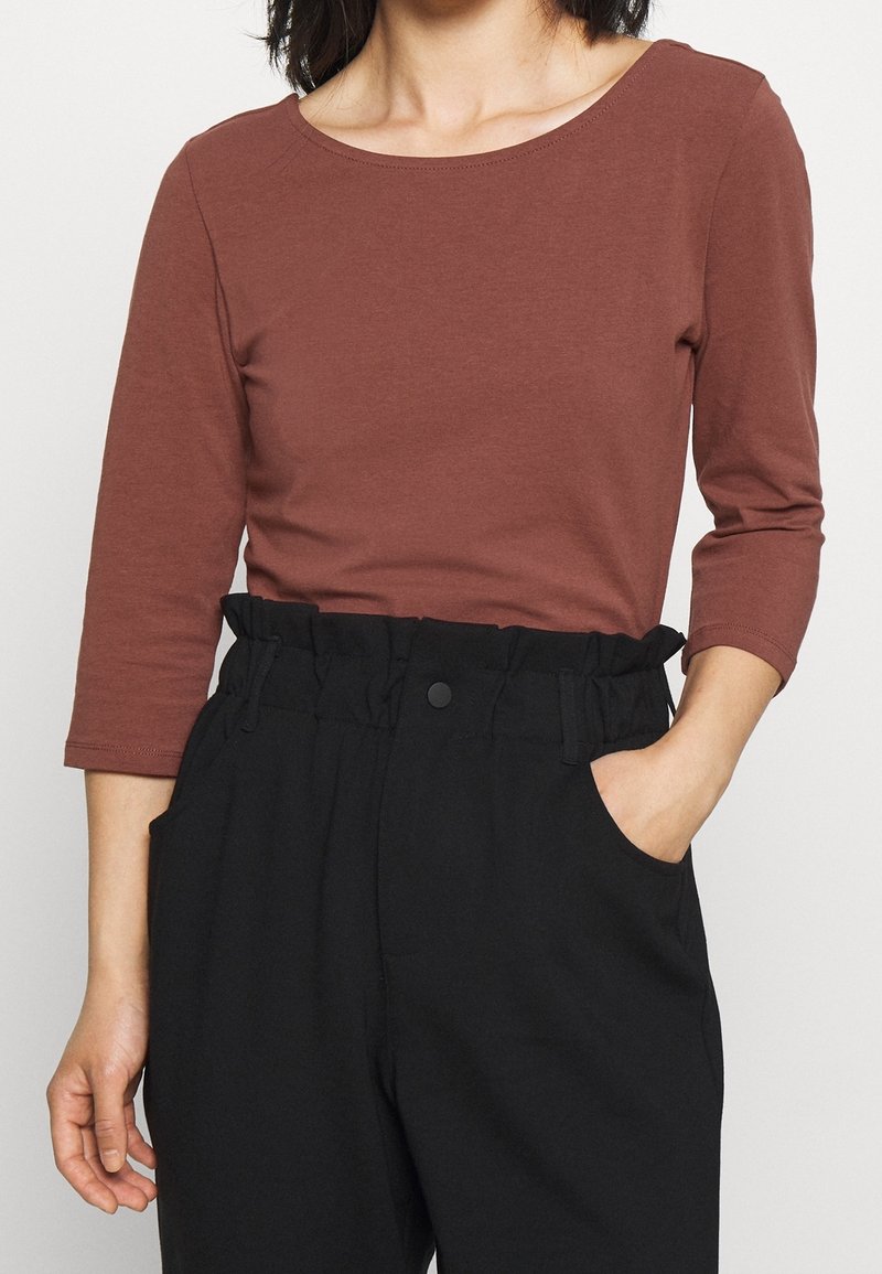 Brązowa, dopasowana bluzka z długim rękawem i dekoltem łódki, połączona z czarnymi spodniami o wysokim stanie z marszczonym paskiem i kieszeniami bocznymi.