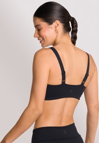 Zwarte sportbeha met brede bandjes, verstelbare hardware, soepel stof en een minimalistisch ontwerp, dat een schone rugprofiel toont.