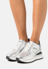 Baskets métalliques argentées avec des accents en mesh et cuir, dotées d'un talon texturé, de lacets blancs et d'une semelle en caoutchouc noire.