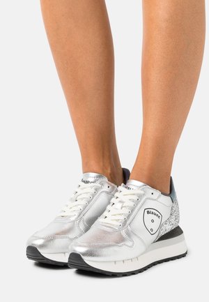 Zapatillas deportivas metálicas plateadas con detalles de malla y cuero, con un talón texturizado, cordones blancos y suela de goma negra.