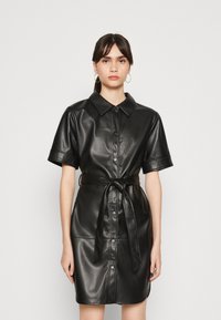 Zwarte faux leren jurk met korte mouwen, knoopsluiting aan de voorkant en een bijpassende strikriem in de taille. Gladde textuur en gestructureerd ontwerp.