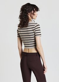 Top accollato e aderente color beige con righe orizzontali nere; abbinato a pantaloni sartoriali marrone scuro. Tessuto liscio, maniche corte e design minimalista.