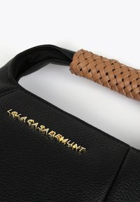 Black leather handbag with a braided tan handle and gold logo detail, featuring a textured surface and minimalistic design.