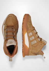 Tummanruskeat samettiset ja verkkomaiset lenkkarit, joissa on kumipohja. Kenkien sivuilla on kolme valkoista raitaa, ja ne voit pukea nauhojen avulla. Takana on vetonauha.