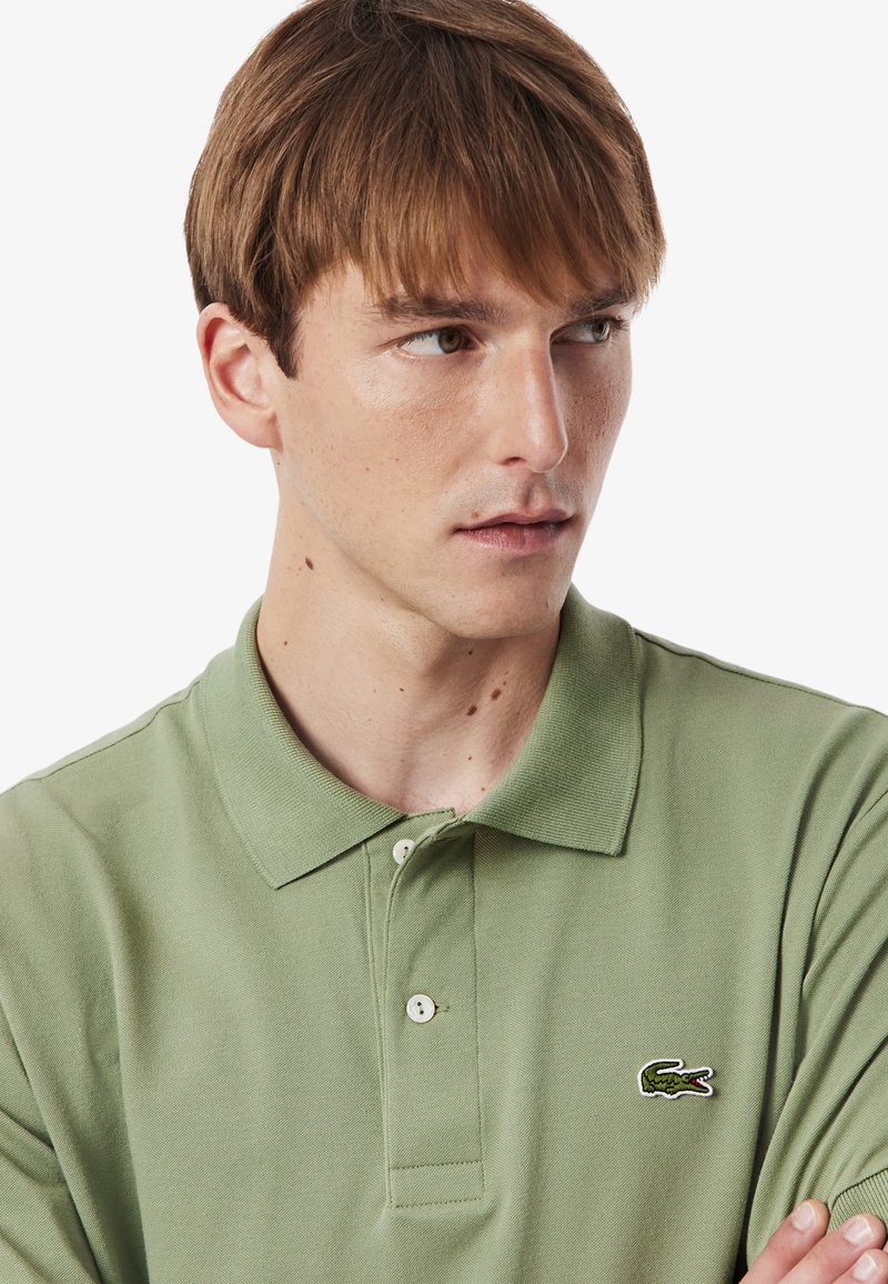 Light green polo shirt made of cotton, featuring a classic collar, two buttons, and a small embroidered crocodile logo on the chest.