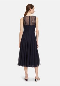 Robe sans manches bleu marine avec un dos transparent, jupe plissée et en matériau en tulle, dotée d'une fermeture éclair dissimulée. Design minimaliste.