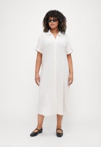 White linen shirt dress featuring a collar, button front, and rolled short sleeves, paired with black strap Mary Jane flats.