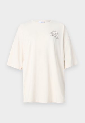 Kremfarget, oversized T-skjorte med korte ermer, liten croissant-grafikk og teksten "Le Croissant" på venstre bryst.