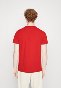 T-shirt rossa in cotone con collo tondo e maniche corte, caratterizzata da un taglio dritto, una texture liscia e un piccolo dettaglio con logo sull'orlo.