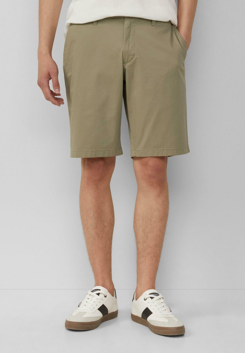 Beige Shorts aus leichtem Material mit geradem Bein, Seitentaschen und sauberem Saum. Kombiniert mit weißen Sneakers mit braunen Akzenten.