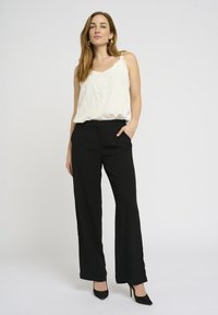 Witte mouwloze top met kantdetail, gecombineerd met zwarte wijde broek en zwarte hoge hakken. Gladde stof en een getailleerde pasvorm.