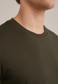 Tricou cu guler rotund de culoare verde măslin, fabricat din bumbac. Are o textură netedă și o croială standard, fără modele sau accente vizibile.