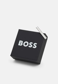 Emballage en boîte noire avec un accent en clip métallique argenté ; possède un logo "BOSS" audacieux en blanc à l'avant, forme carrée, surface lisse.