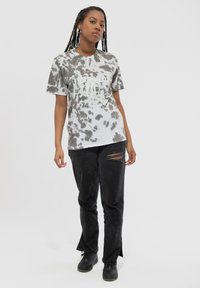 Gray and white tie-dye T-shirt with a graphic print, worn with black jeans featuring distressed detailing and split hems. Black footwear.