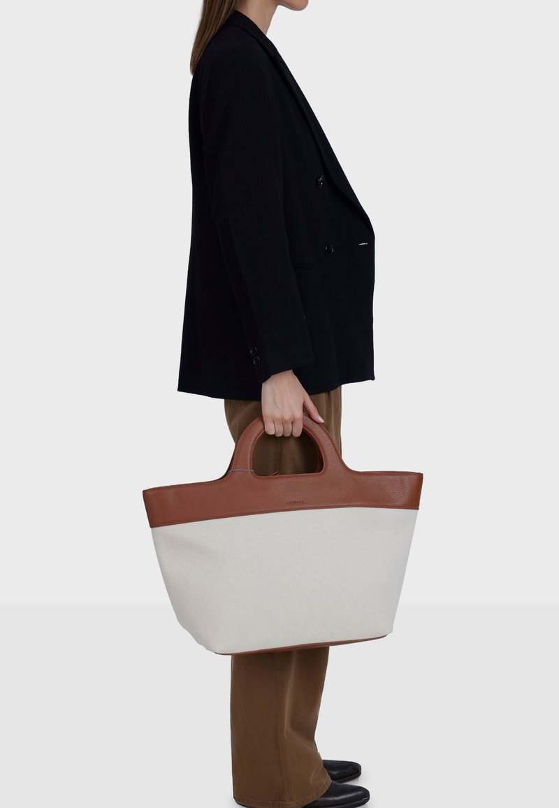 Platnena torba za nošenje s smeđim kožnim detaljima, s naglašenim oblikom, dvostrukim ručkama i kontrastnim krem tijelom. Čist dizajn, prostrana.