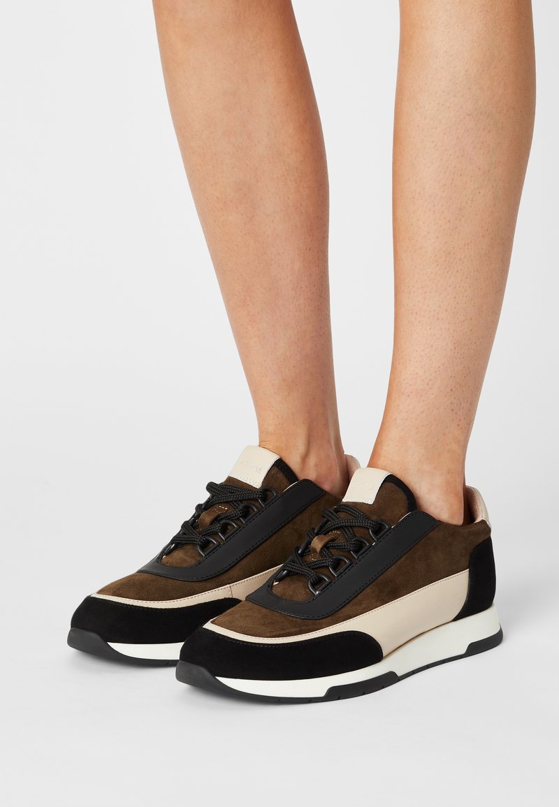 Brązowe i beżowe zamszowe sneakersy z czarnymi akcentami, z okrągłym noskiem, sznurowanym zapięciem oraz białą gumową podeszwą.