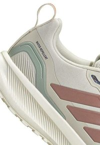 Zapatilla de color gris claro con una parte superior de tela texturizada, detalles en rosa y teal, una suela gruesa blanca y la etiqueta "RESISTENTE AL AGUA" en el lateral.
