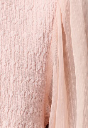 Light pink fabric close-up showing textured knit next to sheer pleated material, highlighting contrasting textures and softness.