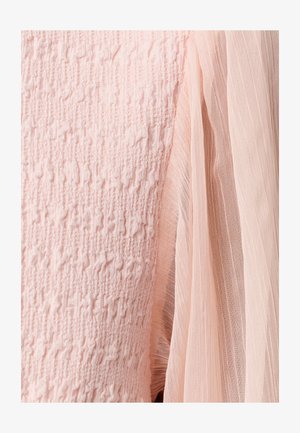 Light pink fabric close-up showing textured knit next to sheer pleated material, highlighting contrasting textures and softness.