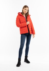 Jachetă roșie tip puffer cu glugă, design matlasat, fermoar frontal, purtată peste un pulover mov, asociată cu blugi strâmți negri și cizme de piele negre cu șireturi.