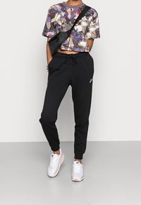 Cropped floral-patterned shirt with short sleeves, paired with black sweatpants featuring an elastic waistband and Nike logo. White and pink sneakers.