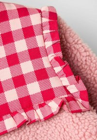 Fleece antklodė su rožiniu, minkštu paviršiumi ir raštuota raukšle raudonai ir šviesiai rožinės spalvos langelių raštu. Kraštai nublukę ir surinkti.
