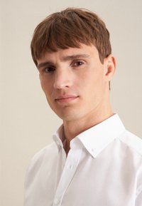 Chemise à col blanc avec un design à boutons, tissu lisse, coupe ajustée et détails de couture subtils, portée par un mannequin masculin.