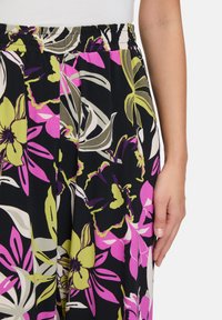Spodnie crop z kwiatowym wzorem i elastycznym paskiem w talii. Kolory to czarny, różowy i zielony w dużych wzorach kwiatowych. Miękki, lekki materiał.