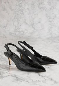 Melna patentā ādas siksniņu kurpe ar asu purngalu, teksturētu krokodilu rakstu, regulējamu sprādzi un šauru, zemu papēdi.