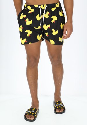 Schwarze Badeshorts mit gelben Gummiente-Mustern und weißem Kordelzug. Schwarze Badesandalen mit gelbem Enten-Design und Logo.