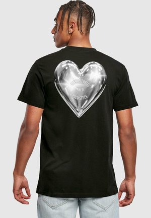Schwarzes T-Shirt mit kurzen Ärmeln, das auf der Rückseite ein glänzendes Herzgrafik und den Text "GROßE GESCHICHTEN BRAUCHEN MUTIGE SCHRITTE" in fetter Schrift zeigt.