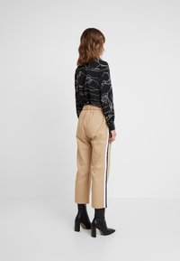 Chemise noire avec motif de lignes de montagne blanches, associée à un pantalon beige avec taille élastique et bandes latérales, et des bottines noires.