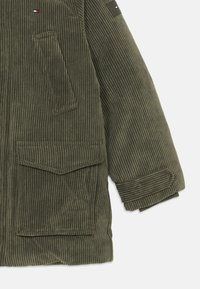 Chaqueta de pana verde oliva con un diseño estructurado, que presenta una textura acanalada, dos bolsillos frontales y puños enrollados para un aspecto entallado.