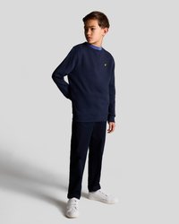 Felpa blu navy con scollo a girocollo e piccolo logo giallo, abbinata a pantaloni coordinati e sneakers bianche. Texture del tessuto liscia.