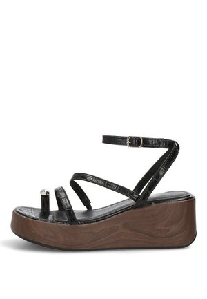 Sandalia de plataforma negra con punta abierta y suela de madera, con tiras delgadas incluyendo una alrededor del tobillo con una hebilla plateada, y una anilla para el dedo del pie con un detalle plateado.