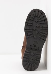 Stivale in pelle marrone con una suola in gomma nera robusta, caratterizzata da profonde scanalature e il logo Timberland, visto dal basso.