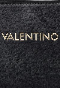 Black textured surface with gold metallic uppercase letters spelling "VALENTINO" centered horizontally.