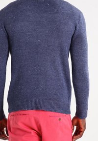 Maglione lavorato a maglia blu navy con maniche lunghe, tessuto strutturato e orlo a costine. Indossato con pantaloni rosa, mostrando la vista posteriore.