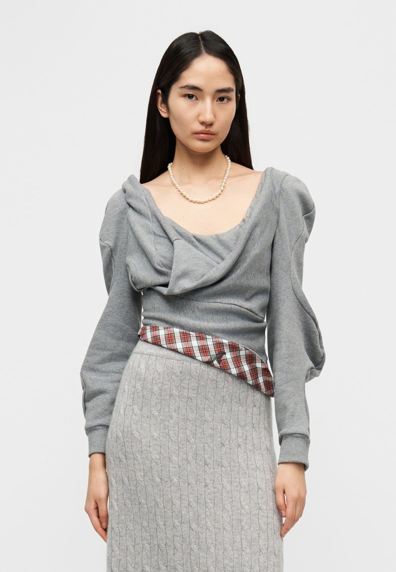 Γκρι φούτερ με ντραπαρισμένο λαιμό και φουσκωτά μανίκια, σε συνδυασμό με γκρι πλεκτή φούστα που έχει καρό λεπτομέρεια στη μέση.