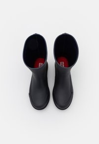 Une paire de bottes en caoutchouc noires à bout arrondi, vues de dessus sur un fond blanc, montrant des semelles intérieures rouges.
