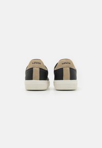 Zapatillas de cuero negro y ante beige con suelas de goma blanca, que presentan un logo negro en el talón y una textura suave.
