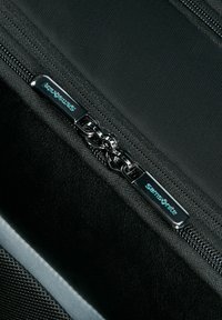 Black fabric suitcase close-up featuring a smooth zipper, glossy metal hardware, and a branded zipper pull with "Samsonite" logo.