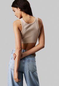 Top corto de canalé beige con amplios escote para los brazos, combinado con jeans de tiro alto en azul claro. Textura suave, diseño minimalista y un sutil detalle en la parte posterior.