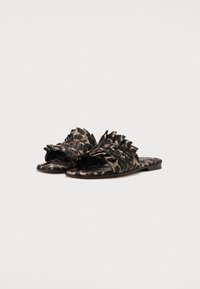Sandales à glissière avec motif camouflage en noir et beige, dotées d'accents en couches ressemblant à des volants et d'un design à bout ouvert sur une semelle plate.