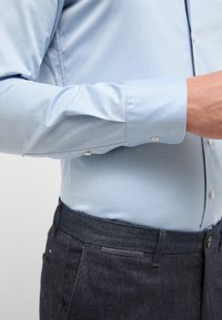 Lichtblauw overhemd met lange mouwen, een soepele textuur, knopenmanchetten en een getailleerd ontwerp, gecombineerd met donkerdenim broek met een subtiel logo.