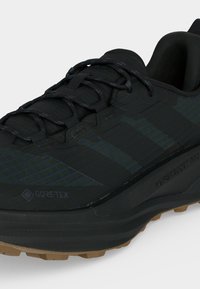 Μαύρο παπούτσι τρεξίματος Gore-Tex με μπλε ρίγες, κλείσιμο με κορδόνια, επενδεδυμένο περιμετρικά κολάρο και υφασμένο τακάκι σε ταμπά για καλύτερη πρόσφυση.