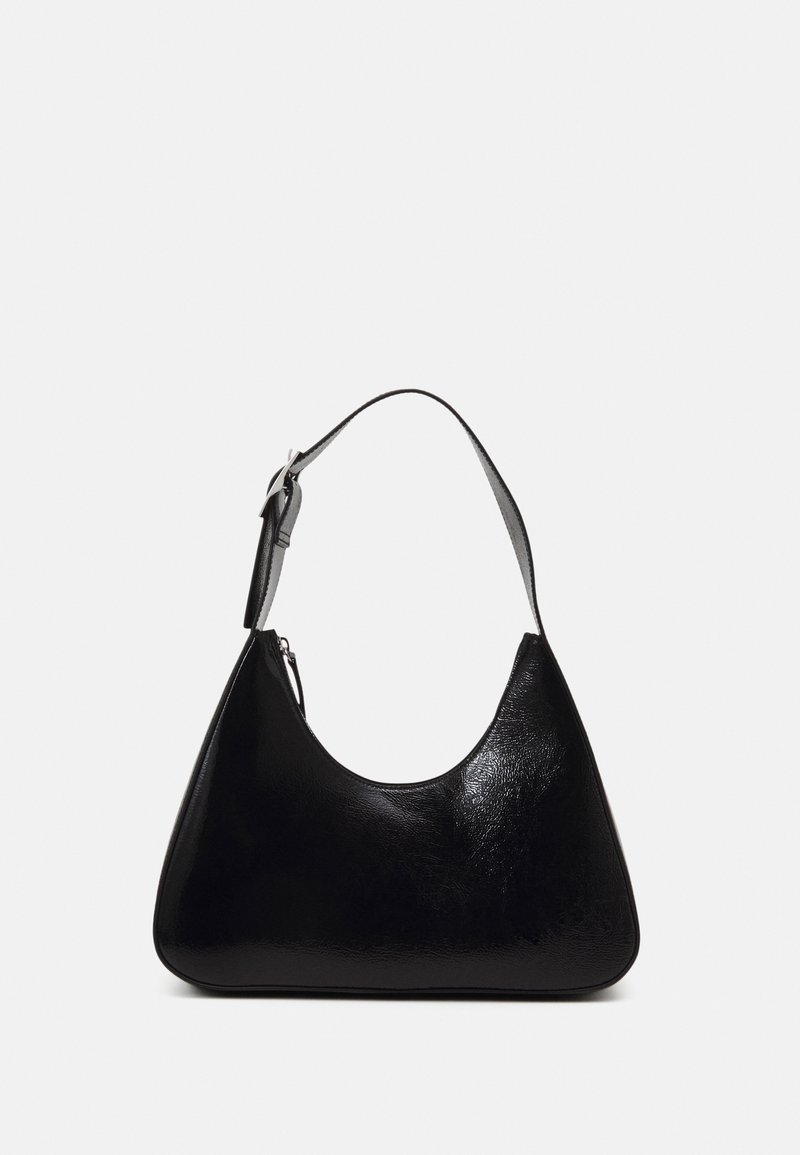Sac à main en cuir noir avec une bandoulière réglable unique et une fermeture éclair, présenté sur un fond uni gris clair.