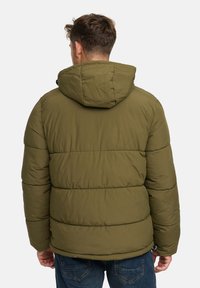 Mand iført en olivengrøn foret jakke med hætte og blå jeans, vist fra ryggen mod en ensfarvet lys baggrund.